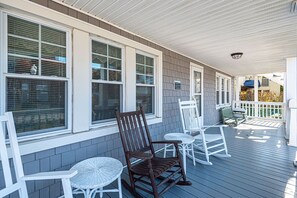 Une véranda couverte, aménagée avec des meubles en osier peints en blanc, notamment des chaises et une table.