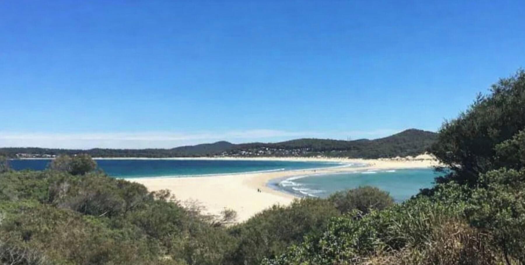 Eine Küstenlandschaft mit Strand, blauem Himmel und fernen Hügeln.