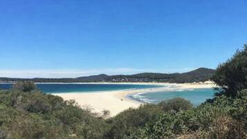 Eine Küstenlandschaft mit Strand, blauem Himmel und fernen Hügeln.