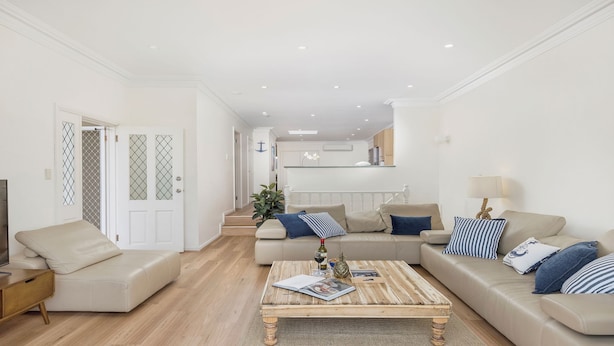 Un salon moderne avec un ensemble de canapés beige, une table basse en bois et un téléviseur posé sur un meuble.