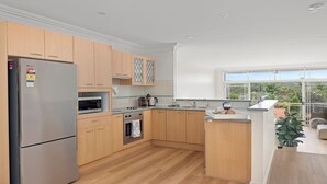 Une cuisine moderne avec des meubles en bois, des appareils électroménagers en acier inoxydable et une grande fenêtre donnant sur l’extérieur.