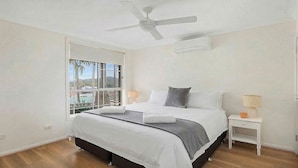 Une chambre à coucher comprenant un lit, un ventilateur de plafond, une fenêtre et une table de chevet avec une lampe.