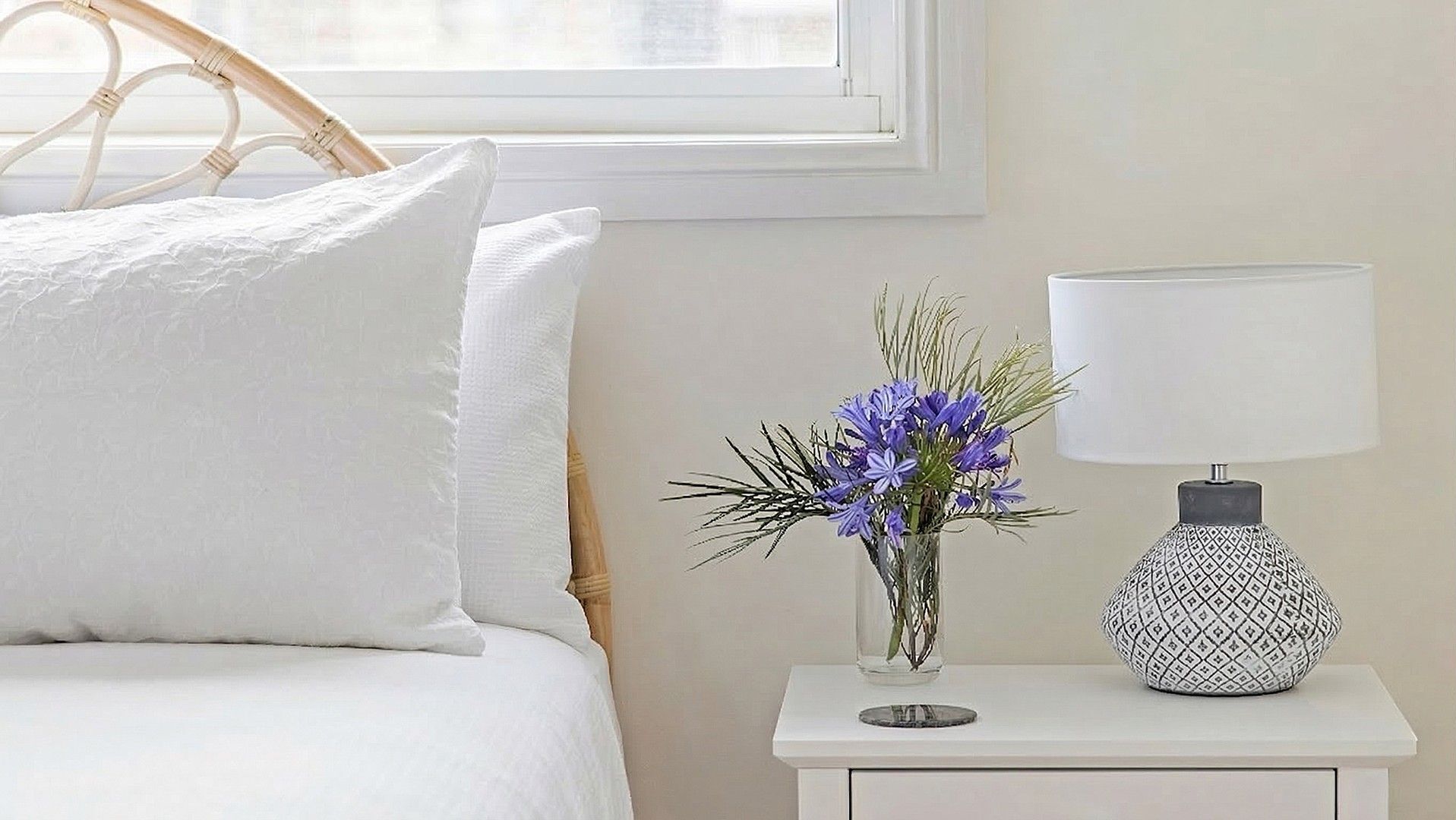 Ein Bett mit weißer Bettwäsche, ein weißer Nachttisch mit Lampe und einem Blumenstrauß.