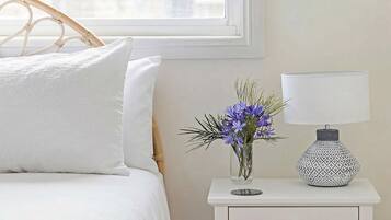 Ein Bett mit weißer Bettwäsche, ein weißer Nachttisch mit Lampe und einem Blumenstrauß.