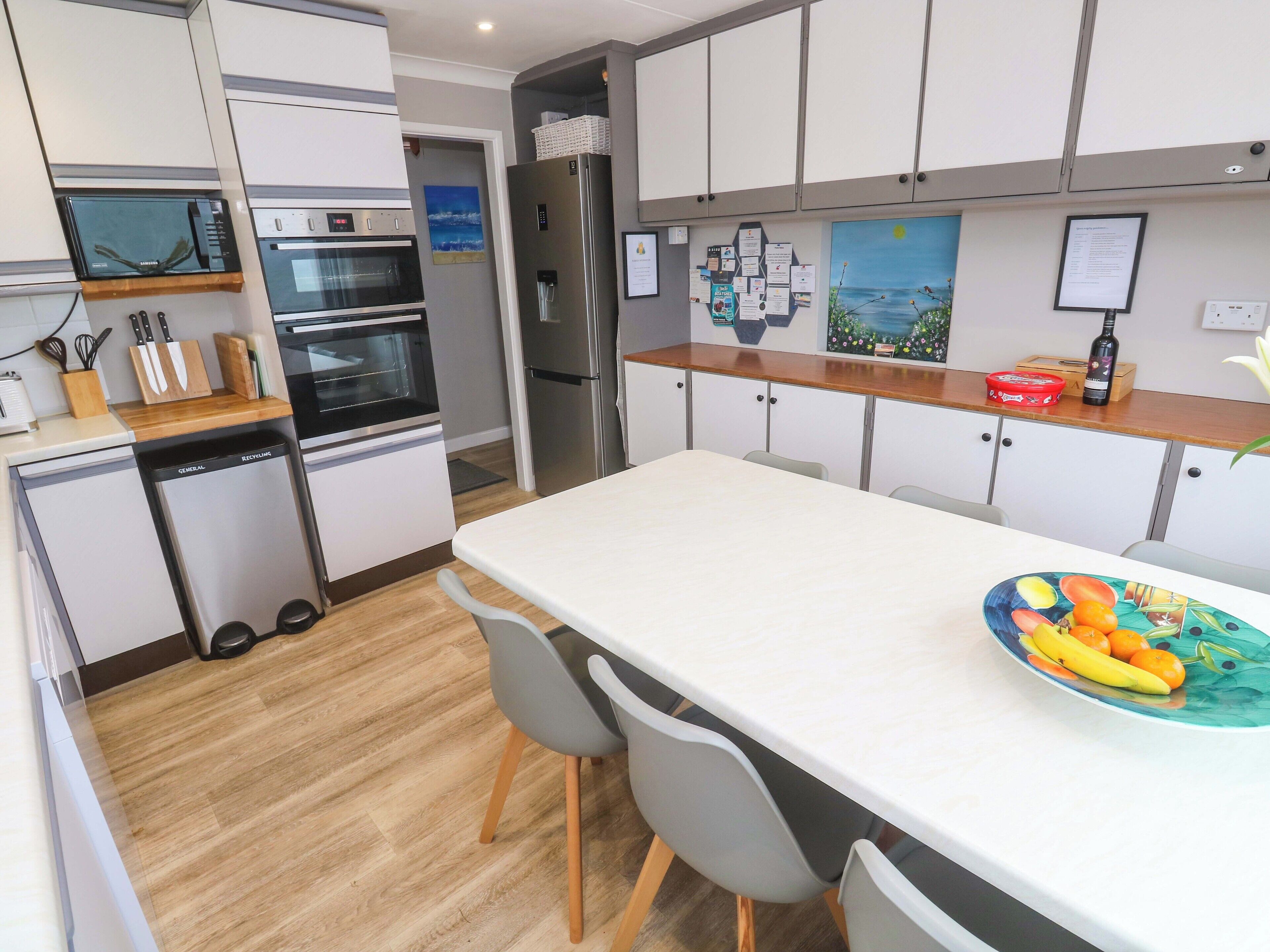 A modern kitchen with white cabinets, a built-in oven, a microwave, and a refrigerator.