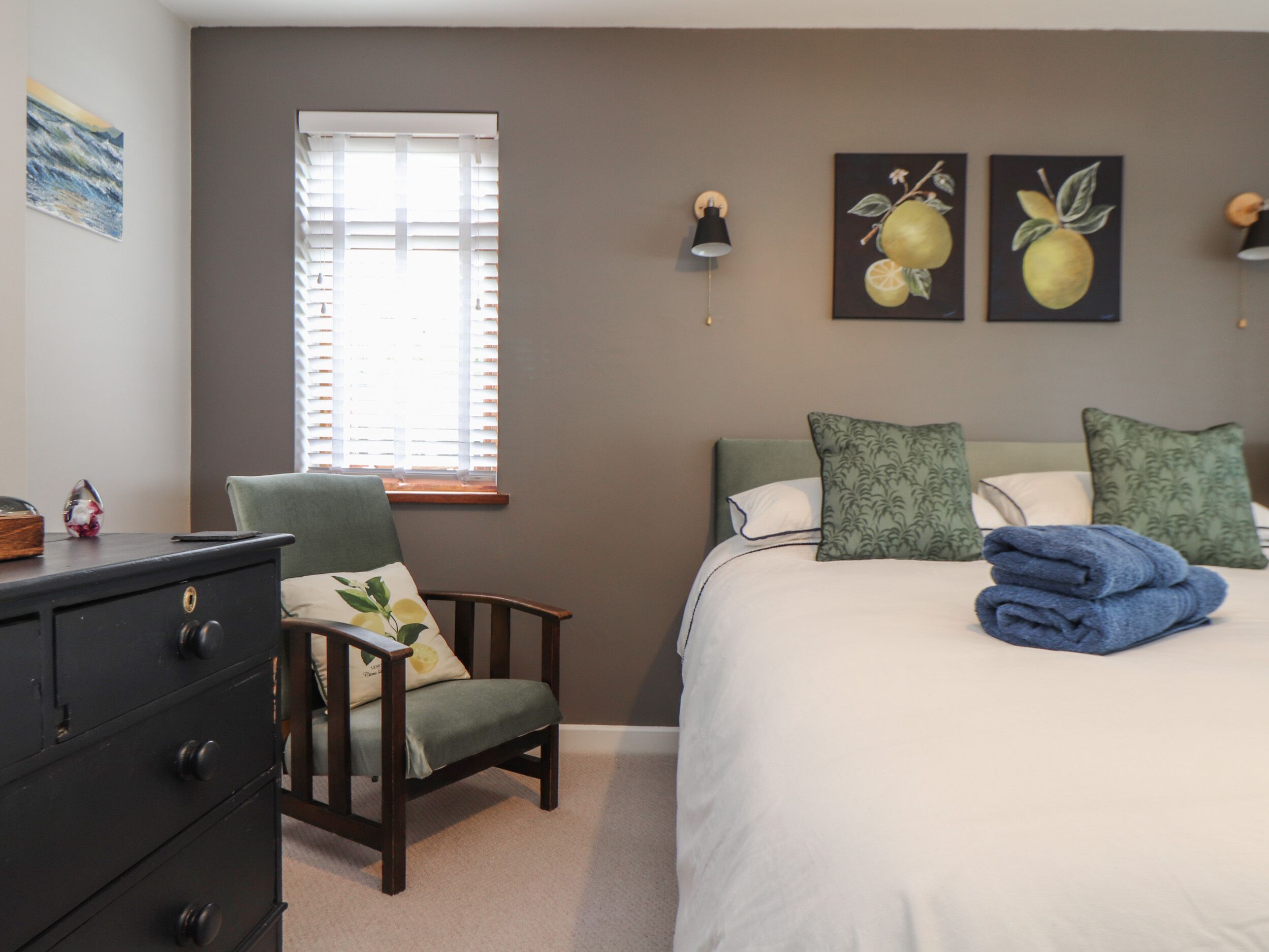 A bedroom with a bed, a chair, a dresser, and artwork on the walls.