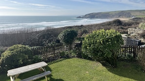 A grassy area with a wooden bench, a stone wall, and a view of the ocean. - Stonecroft (Helston)