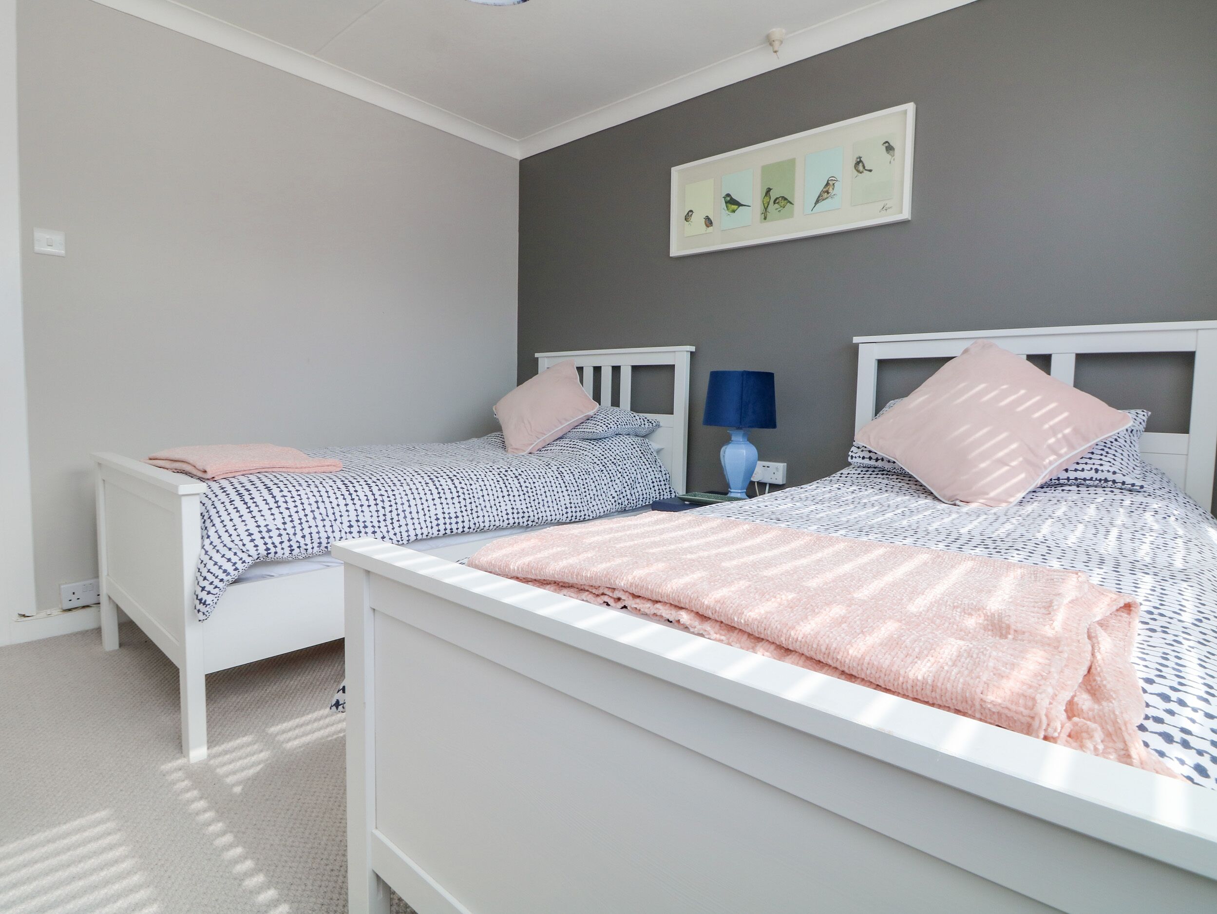 Une chambre avec deux lits simples, une table de chevet avec une lampe et un tableau encadré au mur.