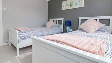 Une chambre avec deux lits simples, une table de chevet avec une lampe et un tableau encadré au mur.