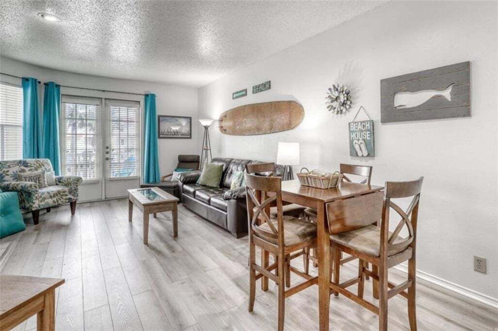 A living room with a sofa, a coffee table, a dining table with chairs, a lamp, and a wall with a fish decoration and a sign that says "BEACH HOUSE".