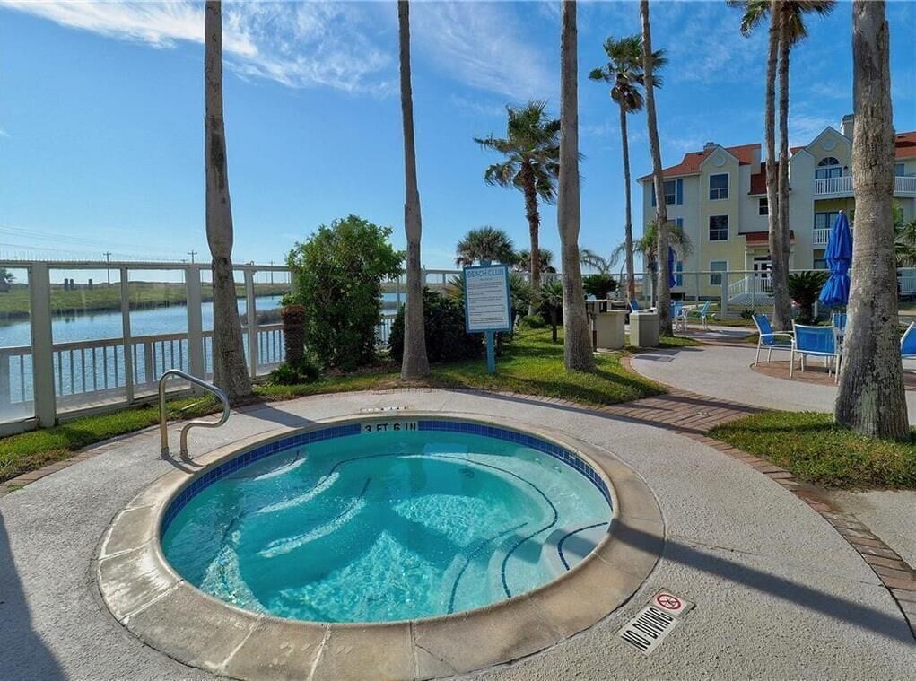 A swimming pool with a sign indicating it is a 'Beach Club' area, surrounded by palm trees and a view of the water.