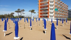 A beachfront hotel with multiple balconies and a sandy beach area with blue umbrellas. - Homely flat with terrace (Porto Santa Margherita)