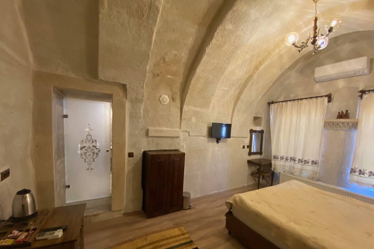 A bedroom with a bed, a wooden cabinet, a television, and a chandelier.