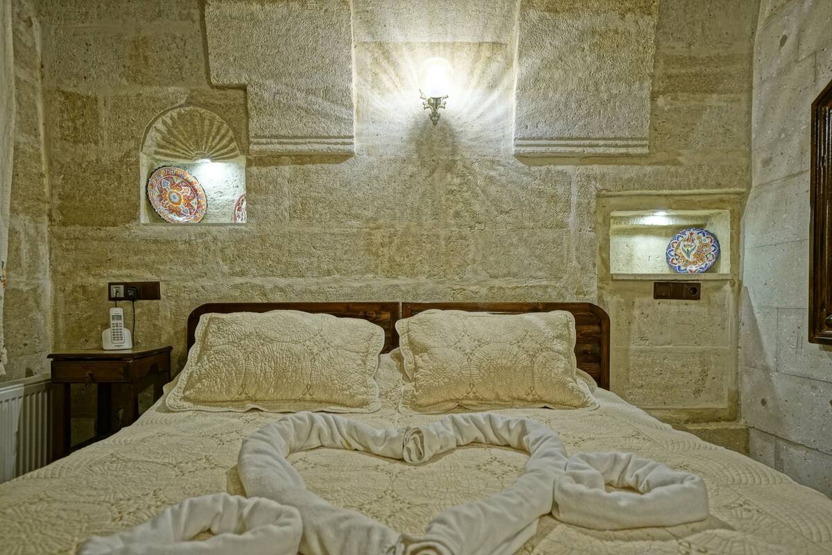 A stone-walled room with a bed, two wall-mounted lamps, and two decorative plates.