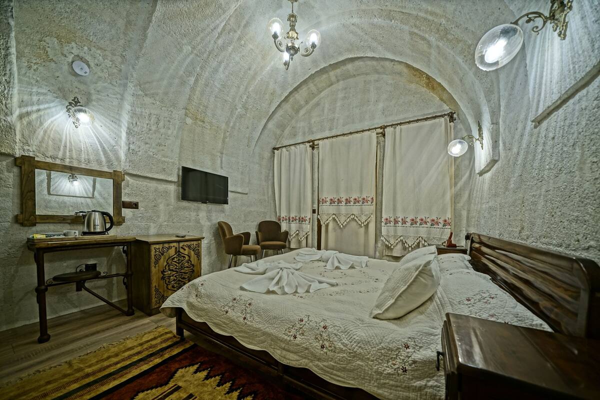 A bedroom with a large bed, wooden furniture, a desk with a kettle, and a television.