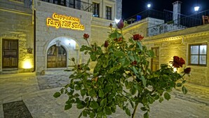 Un bâtiment sur lequel on peut lire l’inscription « Cappadocia Fairy Tale Suites », avec un rosier en premier plan.