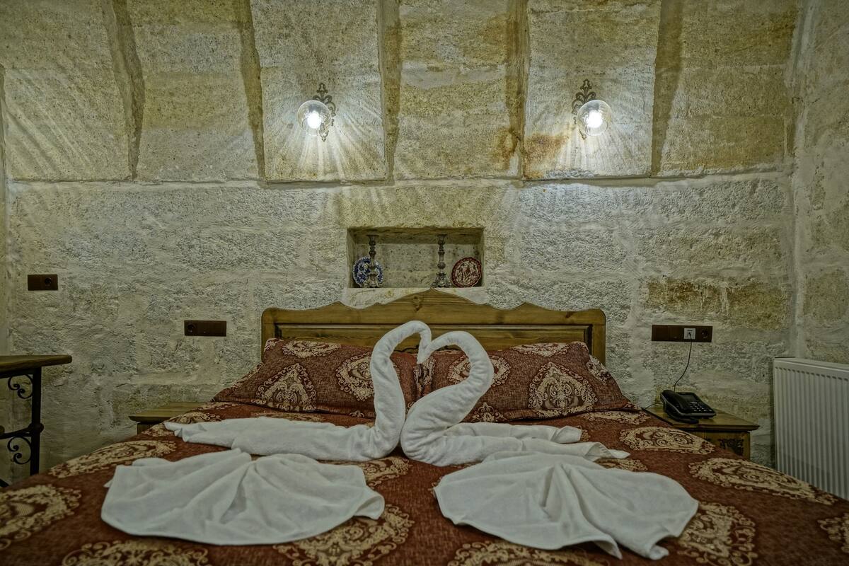 A room with a stone wall, a wooden bed with patterned bedding, and two wall-mounted lights.