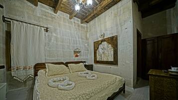A bedroom with a large bed, wooden ceiling beams, a chandelier, and a stone wall.