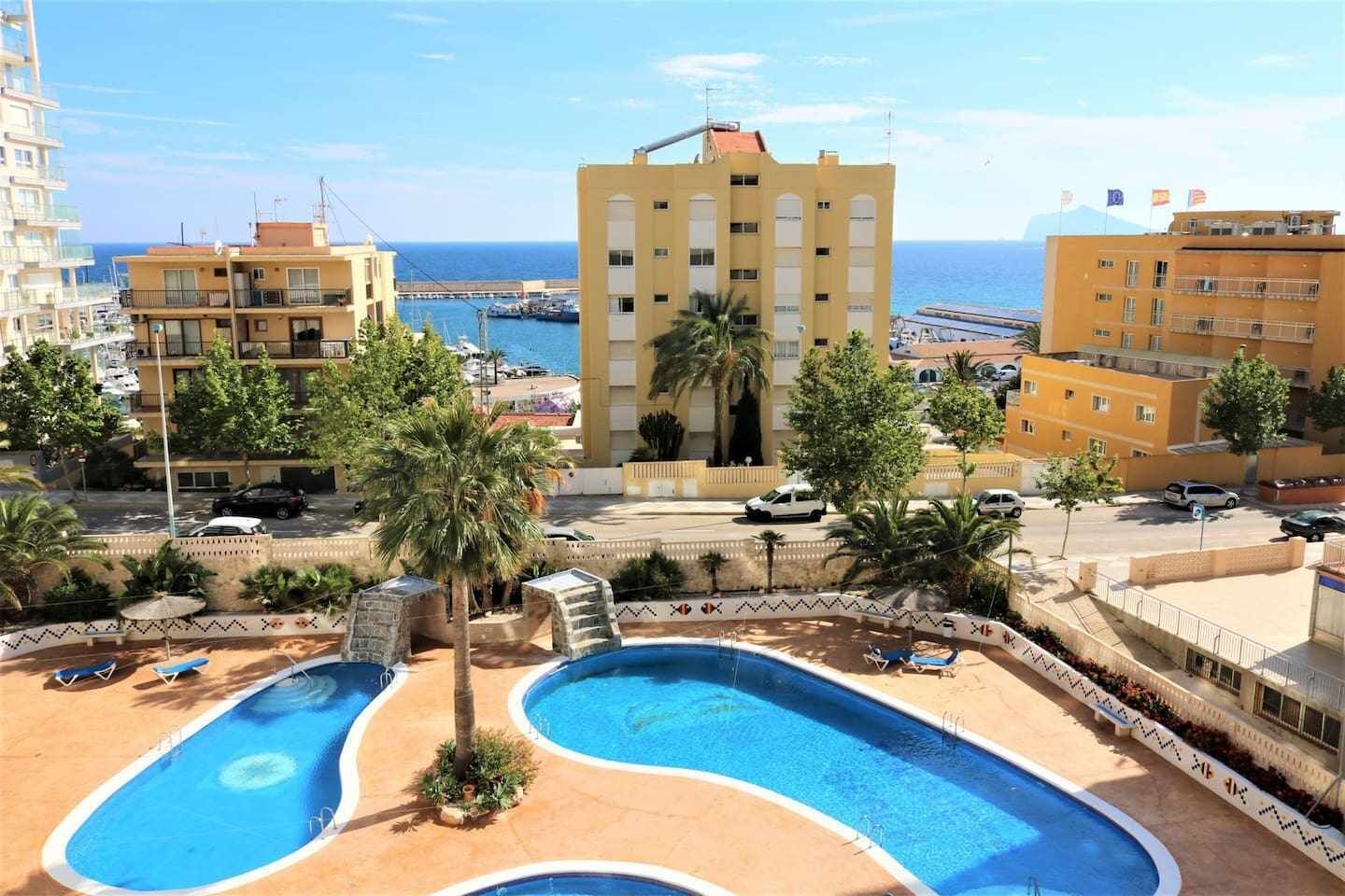 A hotel with a pool area, palm trees, and a view of the sea.