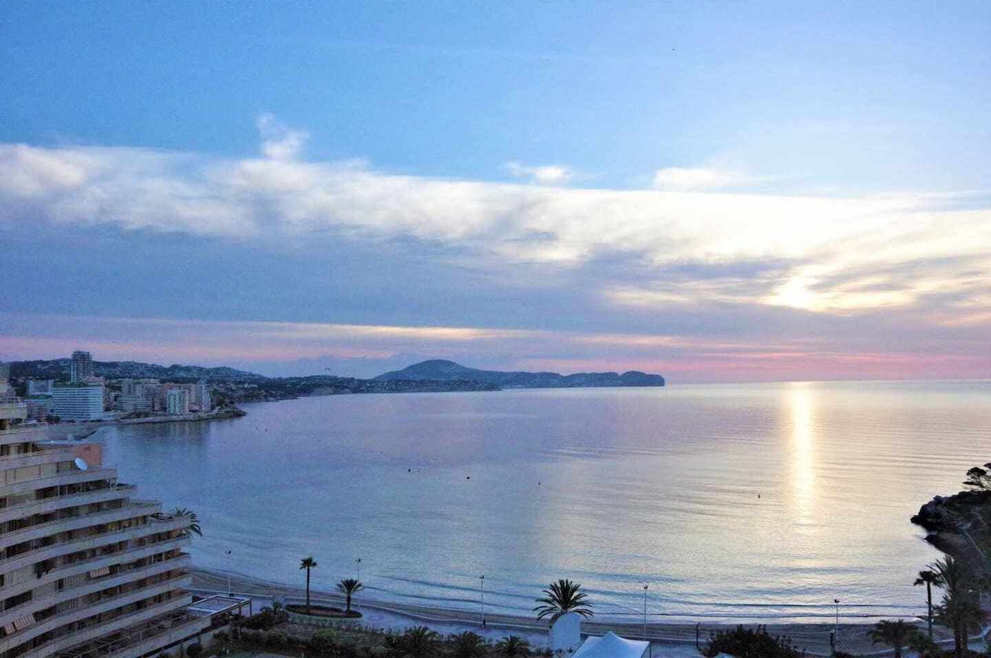 Paisagem costeira com vista para o mar, edifícios e uma montanha distante.