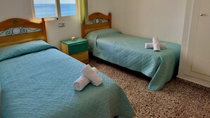 A room with two beds, each with a green bedspread and a rolled towel on top. There is a small wooden nightstand with a lamp between the beds. - 14F SEA II 1 bedroom (Calpe/Calp)