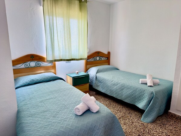 A hotel room with two beds, a nightstand, a lamp, and a window with a curtain. - 14F SEA II 1 bedroom (Calpe/Calp)