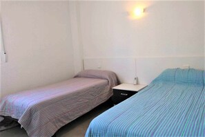 A small, single room with two beds, a nightstand, and a wall-mounted light. - Apartment 48D VORA, 2 bedrooms (Calpe/Calp)