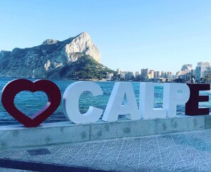 A sign with the word "CALLE" and a heart symbol, set against a backdrop of a coastal cityscape with a prominent mountain. - Apartment 48D VORA, 2 bedrooms (Calpe/Calp)