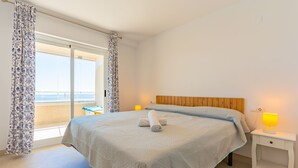 Et soveværelse med seng, natbord, lampe, et vindue med gardiner og udsigt ud