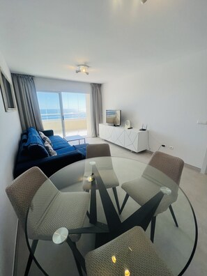 A modern living room with a glass dining table, comfortable seating, a TV, and a view of the beach. - Flat Apolo16 2 bedrooms (Calpe/Calp)