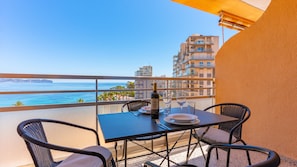 Un balcon avec une table, des chaises, une bouteille de vin et une vue sur l’océan et les bâtiments.