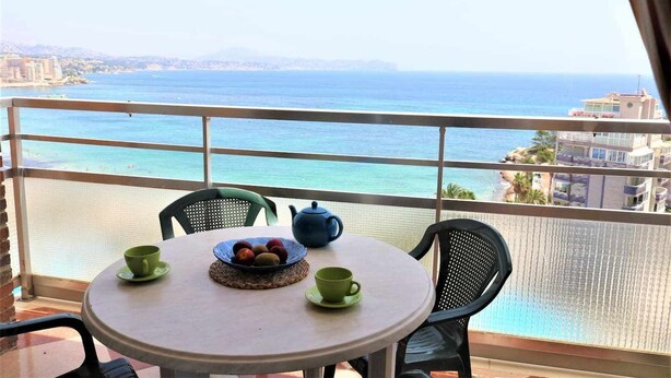 A balcony with a table set for two, a teapot, and a bowl of fruit. The view includes a body of water and distant buildings. - 9A sea views and wifi (Calpe/Calp)