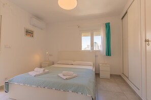 Un dormitorio con una cama, dos mesitas de noche, una ventana con cortinas y una puerta.