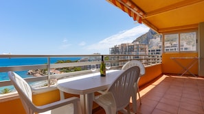 A balcony with a table and chairs, overlooking a coastal view with buildings and a mountain in the distance. - Apartment 510A VORA, 3 bedrooms (Calpe/Calp)