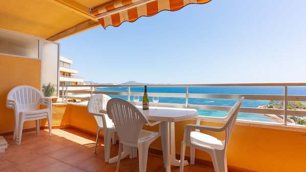A balcony with a table, chairs, and a bottle of wine, overlooking a coastal view.