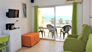 Una stanza con un letto, una scrivania, una televisione, un balcone con sedie e vista sul mare.