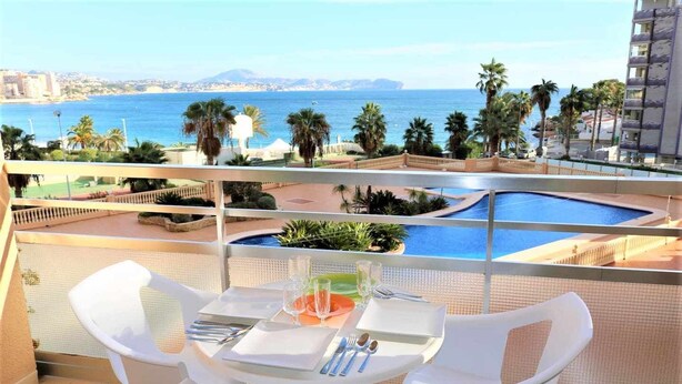 Un balcone con un tavolo apparecchiato per due, con vista su una piscina e sulla costa.