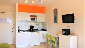 Una cucina compatta con mobili bianchi, un forno a microonde, una macchina da caffè e un piccolo angolo ristoro con due sedie.