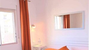 Una camera da letto con un letto, tende arancioni, un comodino bianco con una lampada e uno specchio sulla parete.