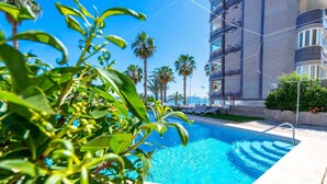 A swimming pool with clear blue water, surrounded by palm trees and a modern building with balconies. - mizzen 84, 3 bedrooms (Calpe/Calp)