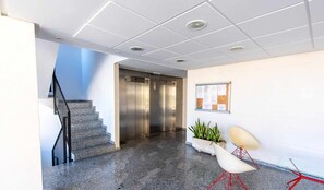 Ein modernes Interieur mit Treppe, Aufzügen, einer Schwarztafel und einer Sitzecke mit Pflanzen.