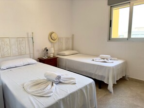 Une chambre d’hôtel avec deux lits simples, une table de chevet avec une lampe, un chapeau et un téléphone.