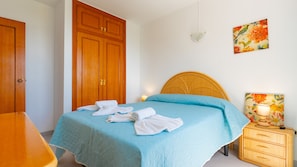 Een hotelkamer met een bed, een houten kledingkast, een nachtkastje en een wandlamp.