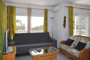 Uma sala de estar com um sofá, uma mesa de centro de vime e uma televisão sobre um móvel.