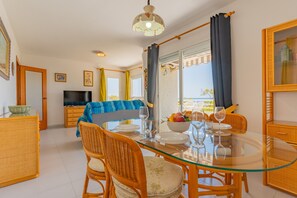 A dining area with a glass table, wicker chairs, and a view of the sea through large windows.