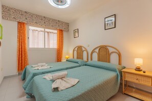 A hotel room with two beds, a window with curtains, a wall-mounted picture, and a bedside lamp.