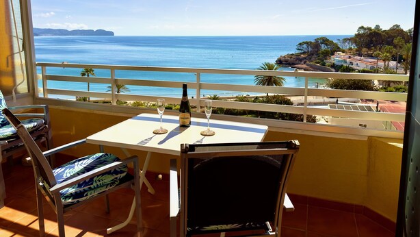 A balcony with a table, two chairs, and a bottle of champagne. The view includes the sea and a distant island. - apartment 46A VORA 2 bedroom (Calpe/Calp)