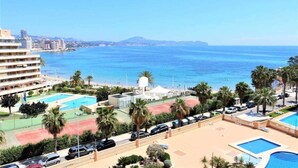 Ett hotell vid kusten med utsikt över havet, en swimmingpool och en tennisbana.