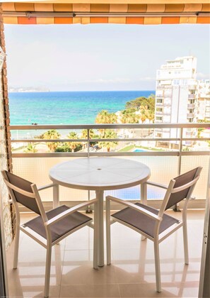 A balcony with a round table and four chairs, overlooking a beach and a cityscape.