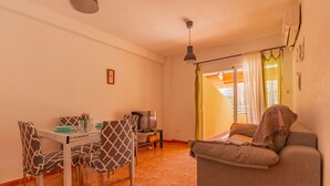 A living room with a sofa, dining table, chairs, a TV, and a window with curtains. - 21C VORA 1 bedroom with sea views and wifi (Calpe/Calp)